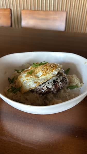 Loco moco-style bowl with a burger patty over rice, topped with a fried egg, gravy, and green onions