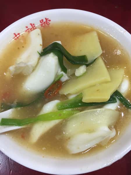 Bowl of Taiwanese seafood soup with squid, bamboo shoots, scallions, and sliced chili