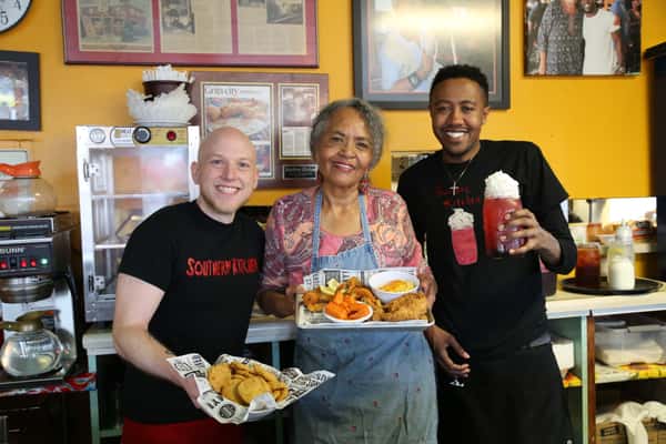 Picture of Gloria holding a plate of food, Ben holding a plate of food, and Tariq holding a lemonade