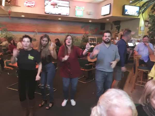 Four friends in a row dancing. Other patrons seated at the bar