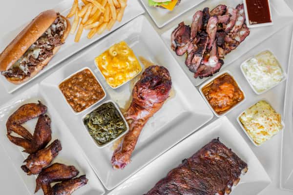 Overhead view of a BBQ spread featuring smoked meats and an assortment of sides arranged on white trays