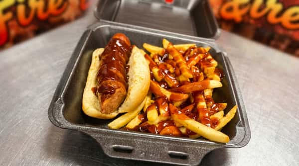 Hot dog in a bun and french fries, both topped with brown sauce, in a gray takeout container.