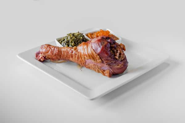 A stuffed smoked turkey leg with herb seasoning on a white plate viewed straight on
