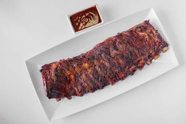 A full rack of smoked BBQ ribs glazed with sauce on a white serving tray
