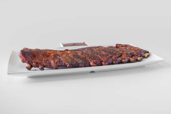 A full rack of smoked BBQ ribs on a white serving tray viewed straight on