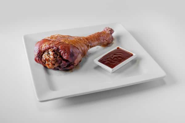 A smoked turkey leg served on a white plate with a side of BBQ dipping sauce