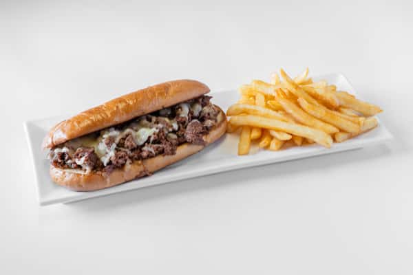 A Philly cheesesteak sandwich on a hoagie roll served with a side of golden french fries on a white plate