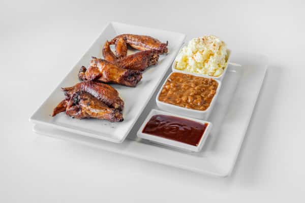 A platter of BBQ chicken wings served with sides of mac and cheese and dipping sauce on a white tray