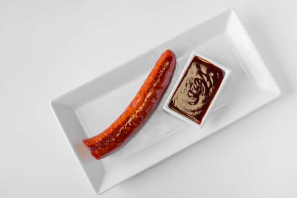 A smoked beef sausage link with a side of dipping sauce on a white plate viewed from above