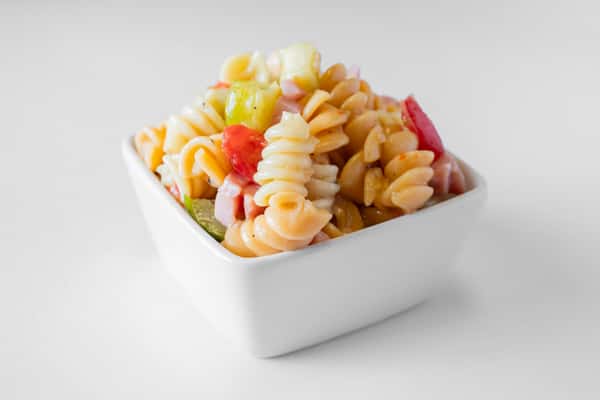 A close-up of a white bowl filled with colorful pasta salad with vegetables