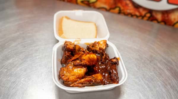 BBQ chicken wings and a slice of white bread in a white takeout container.