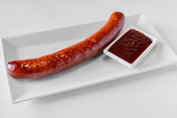 A smoked pork sausage link served on a white plate with a side of BBQ dipping sauce