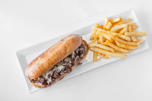 A Philly cheesesteak sandwich on a hoagie roll served with golden french fries on a white plate
