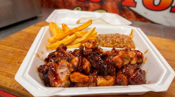 BBQ chicken, french fries, and baked beans in a white styrofoam container, with white bread in background.
