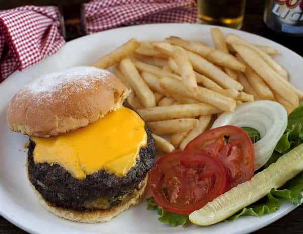 Cheeseburger with tomato, lettuce, onion and a pickle on the side as well as a side of french fries.