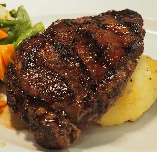 Steak on top of mashed potato with a side of mixed vegetables.