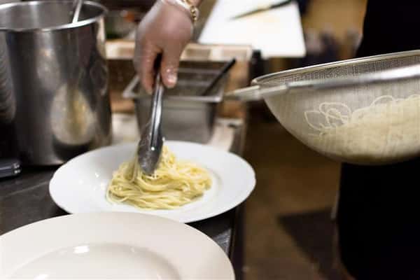 Chef taking spaghetti out of colander and placing it onto a plate.