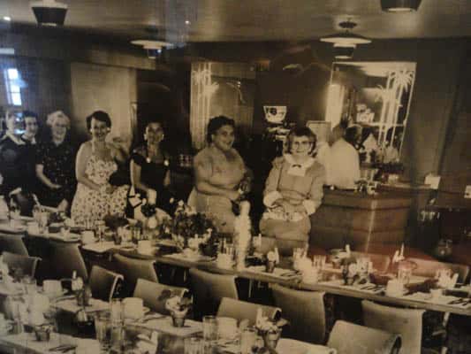 Old black and white image with five women standing in the dining area