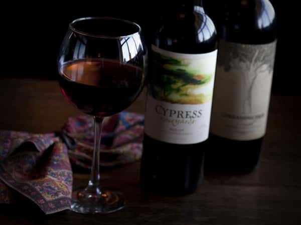 Two bottles and a glass of red wine on a wooden table.