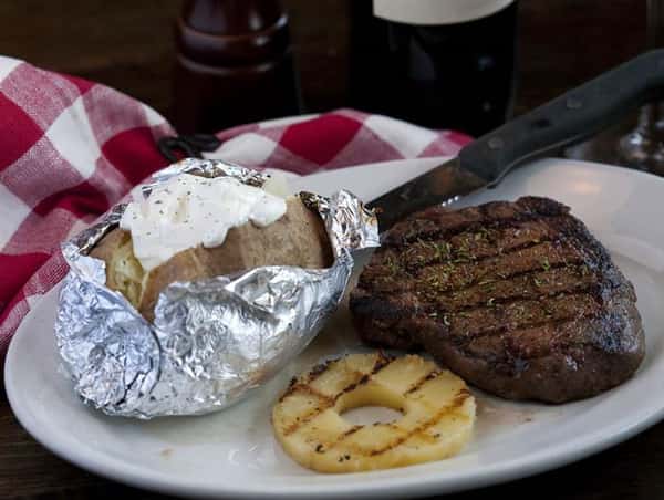 Steak on a plate with a baked potato on the side that is topped with sour cream.