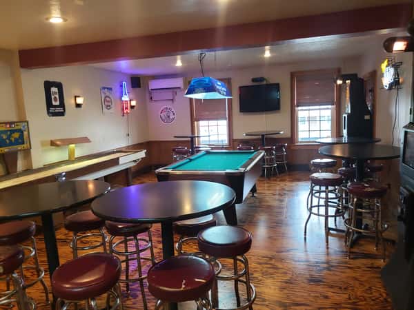 John Hoover Inn game room interior featuring a green pool table, shuffleboard, dark high-top tables, and maroon bar stools on a wood floor.