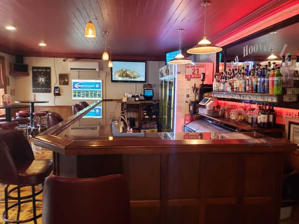 Dark, wooden bar interior at The John Hoover Inn, featuring maroon seating, red ambient lighting, and a well-stocked back bar with liquor bottles.