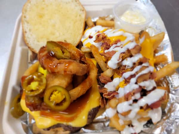 Spicy cheeseburger topped with onion rings and bacon-loaded fries in a takeaway container from The John Hoover Inn.