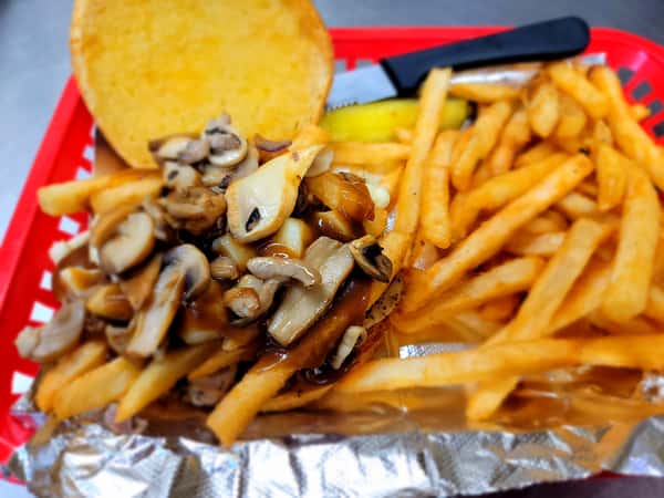 A mushroom gravy-covered sandwich with golden fries and a bun served in a red basket on aluminum foil at The John Hoover Inn.