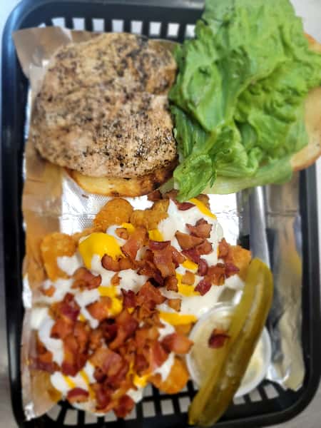 Grilled chicken breast sandwich and bacon-ranch loaded fries combo with a pickle spear, served in a black basket at John Hoover Inn.