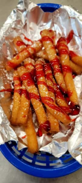 Golden sweet dessert fries drizzled with bright red glaze and powdered sugar, served in a blue basket at The John Hoover Inn.