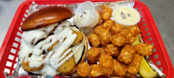 A burger topped with cheese, fried pickles, and drizzled with ranch sauce