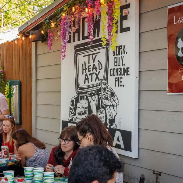 Outdoor pizza patio with mural art, diners enjoying casual restaurant atmosphere under string lights