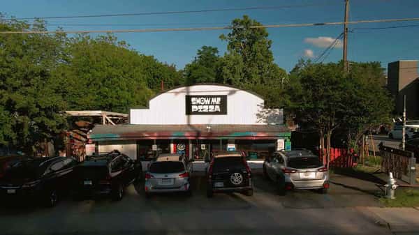 Exterior of Show Me Pizza restaurant with parked cars, casual storefront, and neighborhood setting on a sunny day
