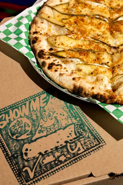 Wood-fired white pizza topped with thinly sliced zucchini, melted cheese, and crispy crust on a colorful textile backdrop