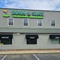 Front exterior of Swing & Slice building with signage for arcade, pizza, and beer above parking spaces.