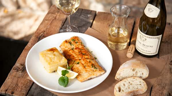 Grilled salmon served with vegetables, bread slices, and a glass of wine.
