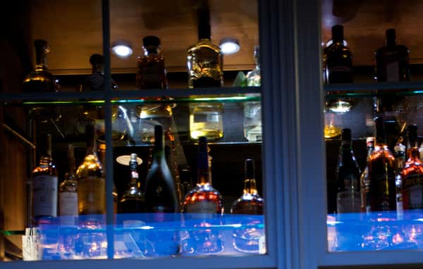 Backlit bar display with bottles of liquor on glass shelves.