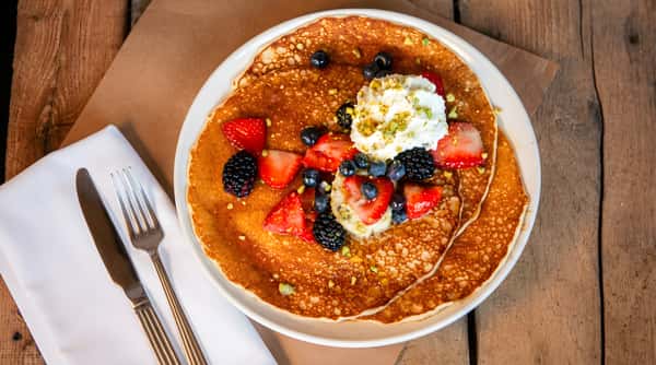 Pancakes topped with mixed berries and whipped cream on a white plate.
