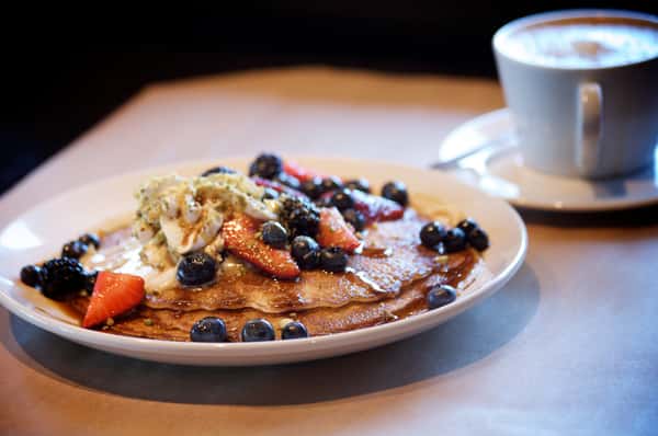 Pancakes topped with blueberries and strawberries served with a cup of coffee.