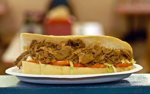 Pulled pork poboy with lettuce and tomato served on a white plate on top of the counter