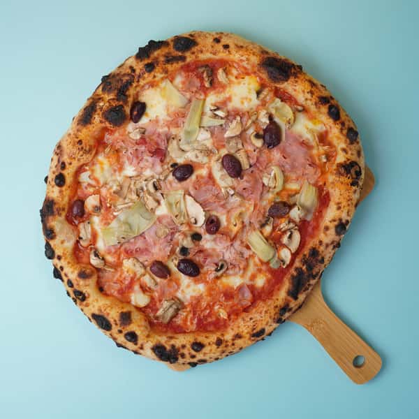 gourmet pizza with ham, olives, mushrooms, and artichokes on light blue background