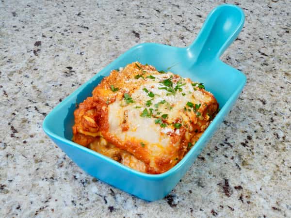 Lasagna served in a blue ceramic dish with a handle, topped with melted cheese and parsley