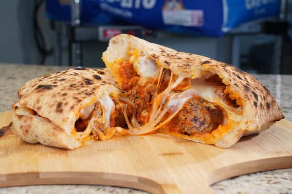 Meatball calzone stuffed with tomato sauce and melted cheese on a wooden board