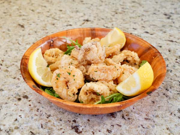 Wooden bowl of crispy fried calamari and shrimp with lemon wedges
