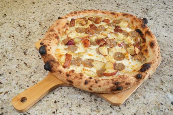 pizza topped with sausage and roasted potatoes on wooden peel over marble surface