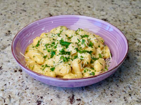 Creamy gnocchi with grated cheese and fresh parsley in a purple bowl