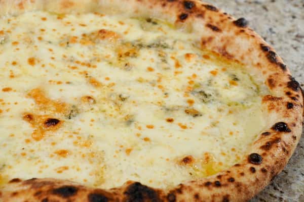 Close-up of a Neapolitan-style four cheese pizza with a bubbly, charred crust and melted cheese blend on a granite countertop.