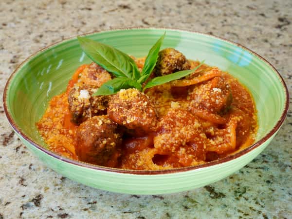 Spaghetti with meatballs and tomato sauce topped with grated cheese and basil in a green bowl