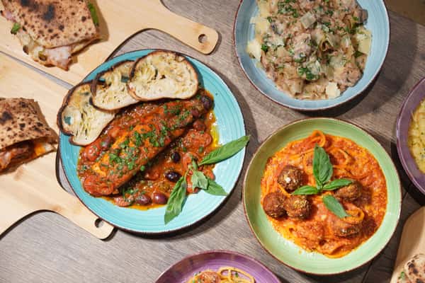 Top view of assorted Italian dishes including meatballs with spaghetti, baked fish in tomato sauce, mushroom pasta, and folded flatbread sandwiches