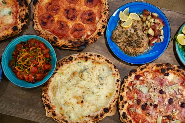 Top view of assorted Italian pizzas including pepperoni, four cheese, and prosciutto with mushrooms, accompanied by pasta, chicken piccata, and roasted potatoes